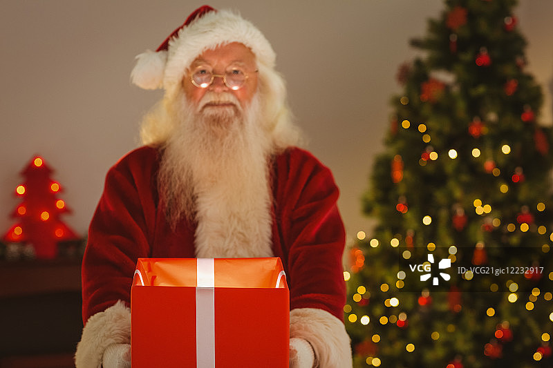 微笑的圣诞老人拿着一个发光的礼物在家客厅图片素材