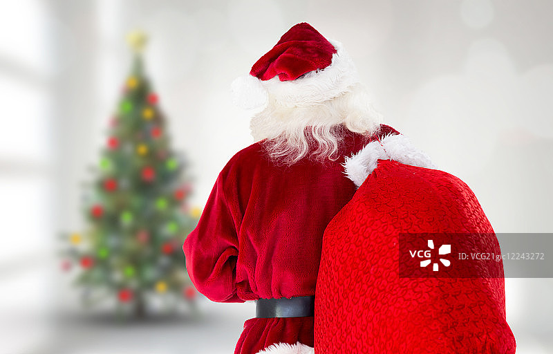 圣诞老人背着袋子抵住房间里模糊的圣诞树图片素材