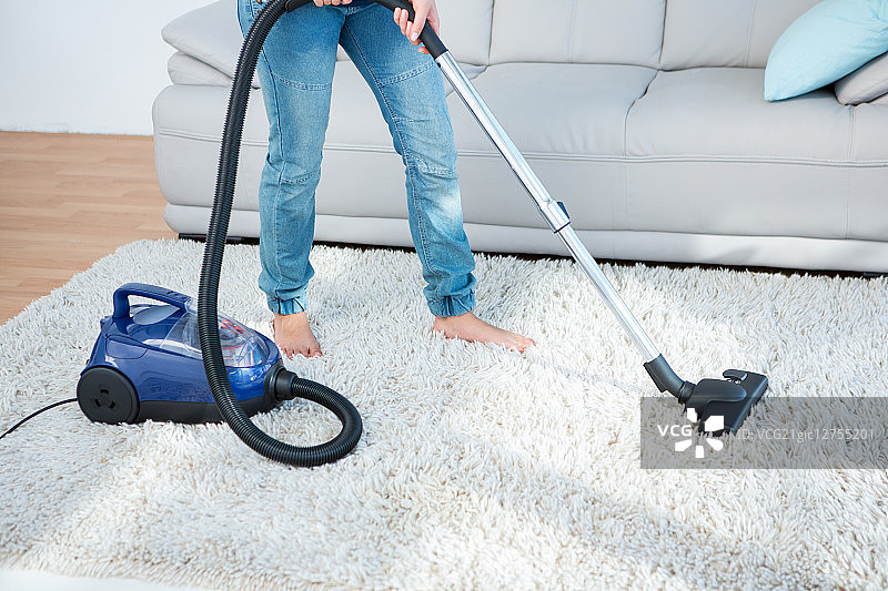 一个女人在客厅的地毯上使用吸尘器图片素材