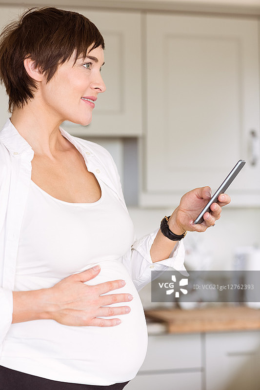一名孕妇在厨房里使用智能手机图片素材