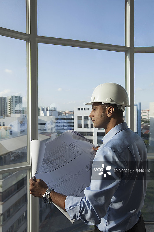 新加坡，男建筑师，戴安全帽，透过窗户看建筑平面图图片素材