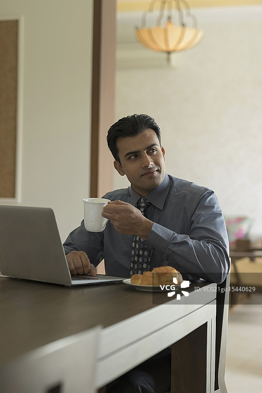 印度，商人在早餐桌上使用笔记本电脑图片素材
