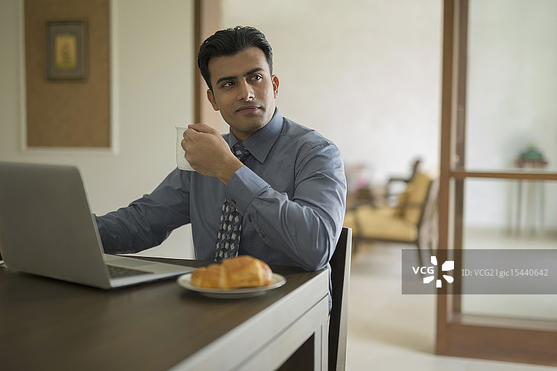 印度，一个拿着咖啡杯坐在家里用笔记本电脑的男人图片素材