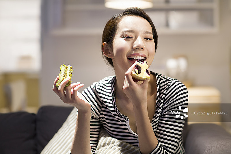 快乐的年轻女子在沙发上吃蛋糕图片素材