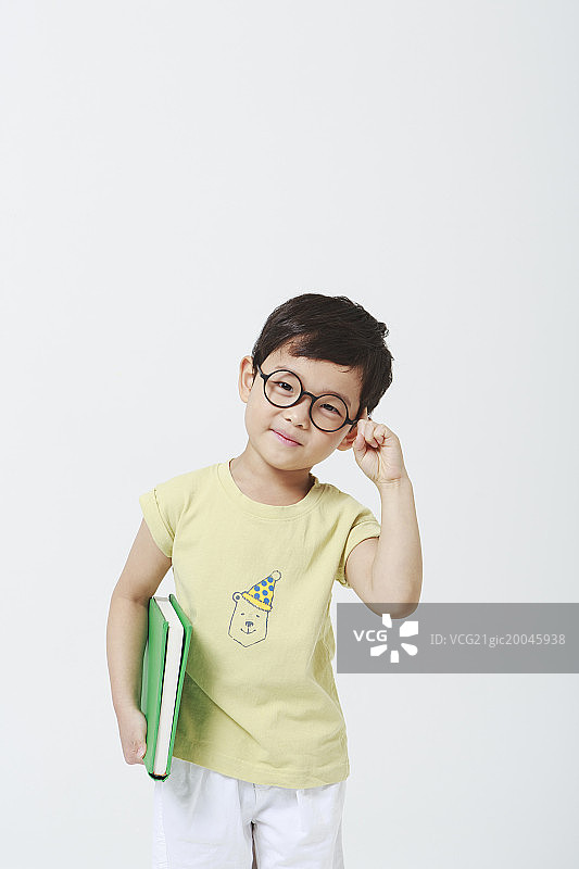 一个小男孩，他的食指在头上戴眼镜，拿着书图片素材