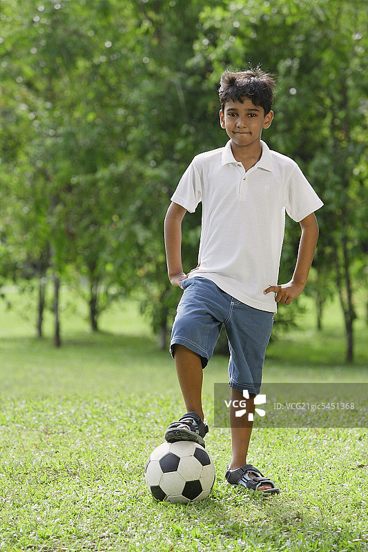 一个小男孩看着摄像机，脚搁在足球上图片素材