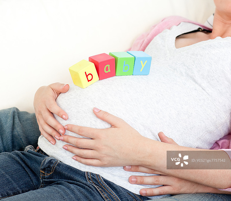 一个怀孕的女人与婴儿立方体在她的肚子和她的丈夫躺在家里的沙发上的特写图片素材