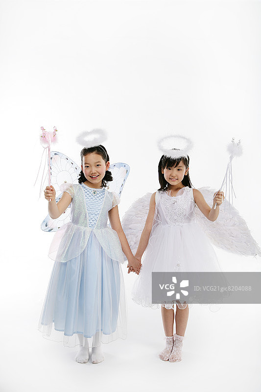 两个女孩(12-13岁)穿着仙女服装，手持魔杖，微笑着，肖像图片素材