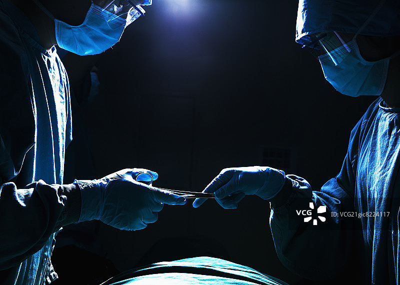 两名外科医生在昏暗的手术室里工作和传递手术设备图片素材