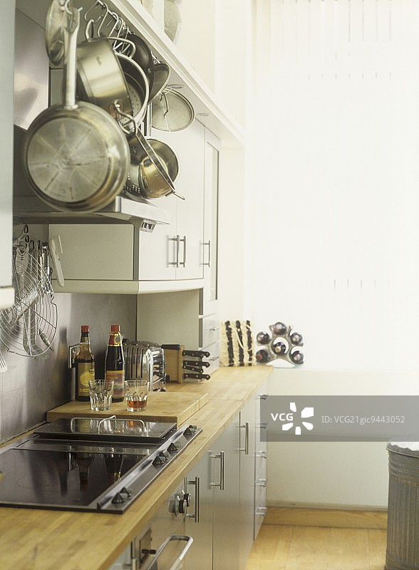 白色墙壁的现代厨房，不锈钢炊具和防溅挡板，陶瓷灶，灰色单元，木制工作台面，图片素材