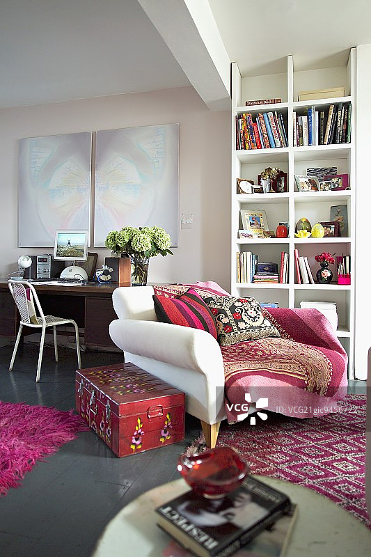 书架前的XXXL椅子，旧写字台上方的现代艺术品——客厅，红色和粉色的地毯和配件图片素材