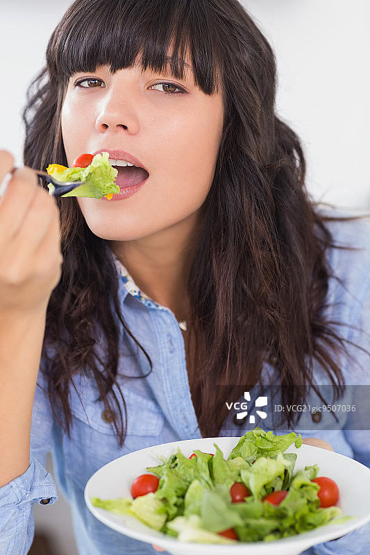 漂亮的黑发女子午餐在厨房吃沙拉图片素材