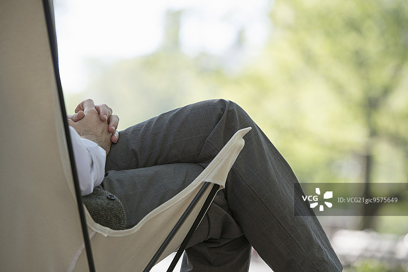城市生活。一个男人坐在公园的帆布野营椅上。图片素材