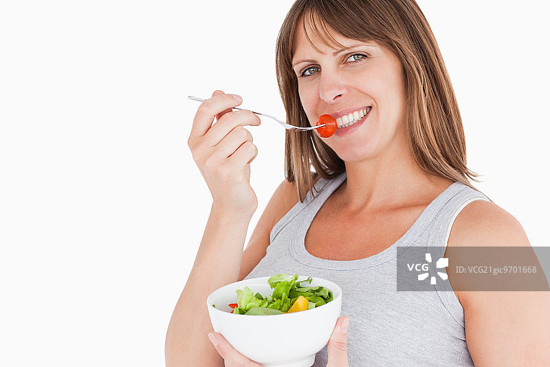 一个漂亮的孕妇拿着一碗沙拉在白色的背景下吃着樱桃番茄图片素材