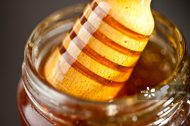 蜂蜜舀出一个罐子，以黑色为背景图片素材