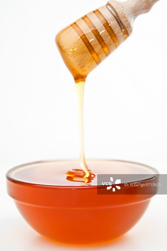 蜂蜜在白色的背景下滴落在碗里图片素材