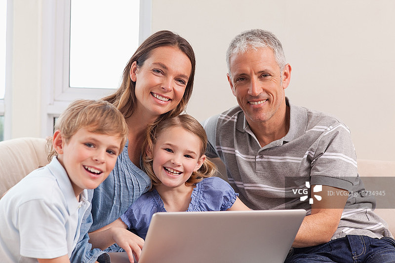 一个幸福的家庭坐在沙发上，在客厅里用笔记本电脑图片素材
