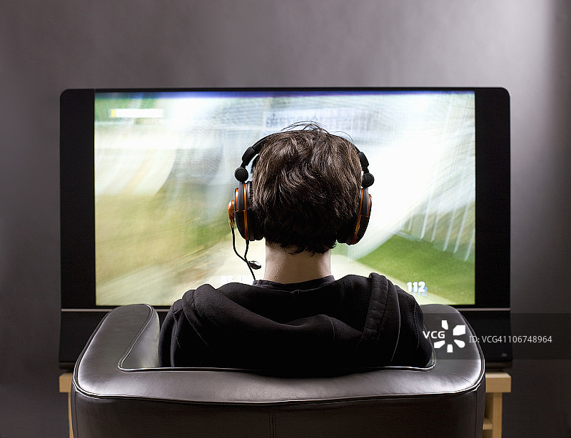 一个十几岁的男孩坐在电视机前玩电子游戏图片素材