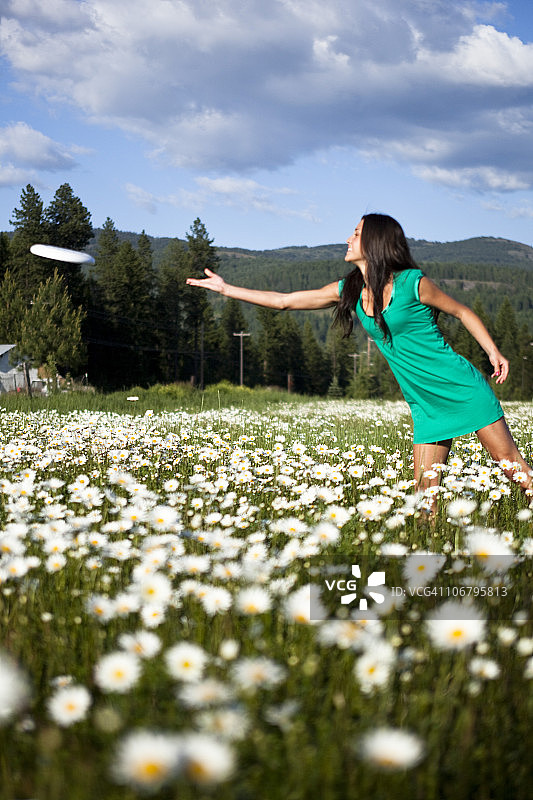 一位美丽的年轻女子微笑着在一片野花丛中扔飞盘。图片素材