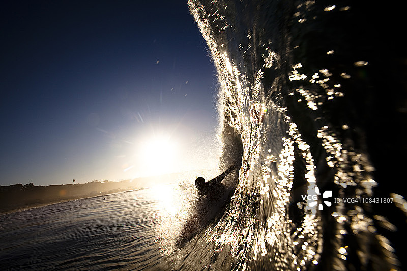 在加州马里布的祖玛海滩，一名男性冲浪者把水伸进了一个桶里。图片素材