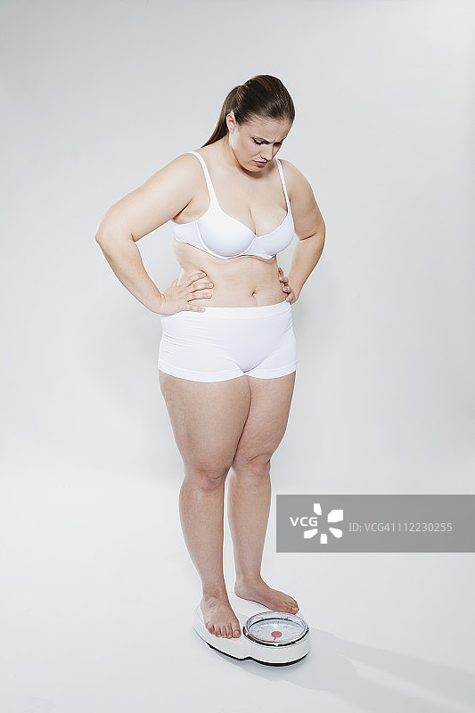 年轻胖乎乎的女人站在浴室的秤上图片素材