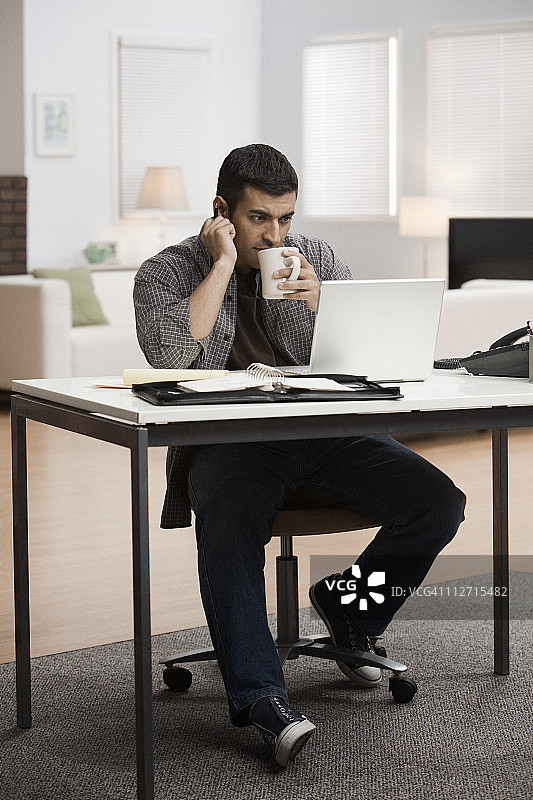 西班牙裔男子在家办公用笔记本电脑喝咖啡图片素材