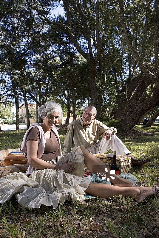 一对成熟的夫妇坐在公园里的野餐毯子上图片素材