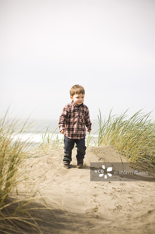 一个男孩在海滩的沙丘上散步。图片素材