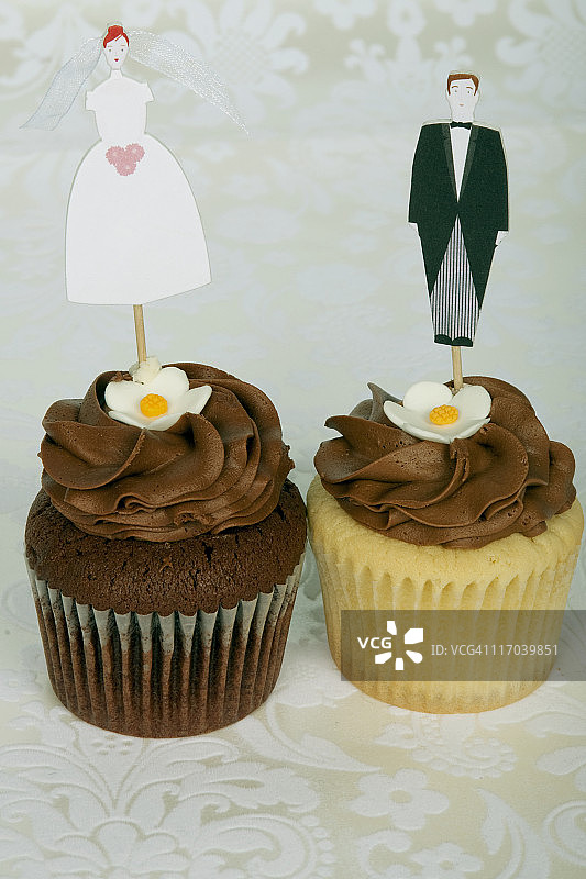 两个纸杯蛋糕，上面有玩具新娘和新郎图片素材