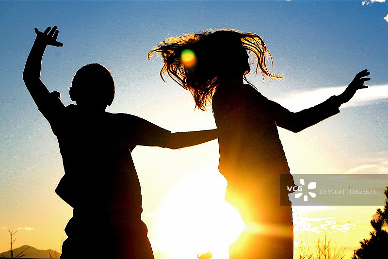 男孩和女孩在夕阳下跳跃的剪影图片素材