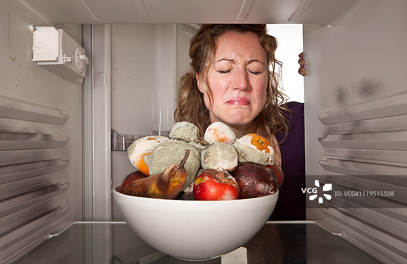 一个女人在冰箱里发现一碗腐烂的水果。图片素材