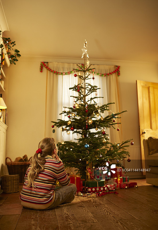 女孩坐在房间里，看着圣诞树。图片素材