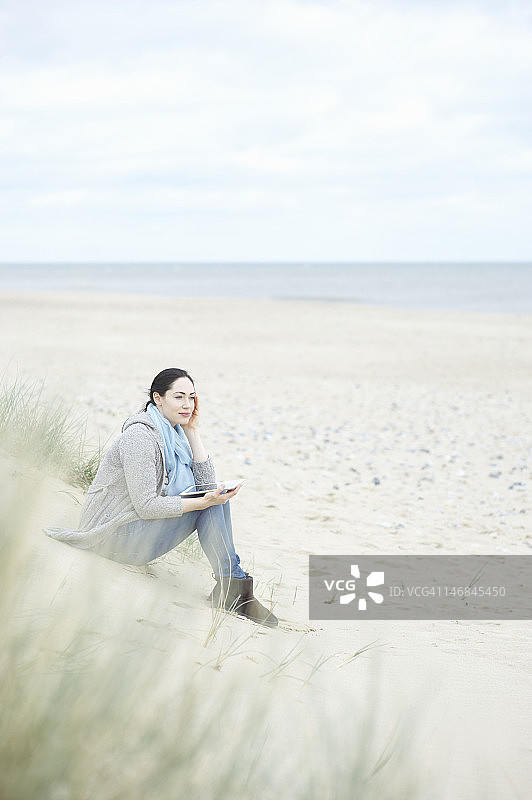 坐在沙滩上拿着平板电脑的女人。图片素材