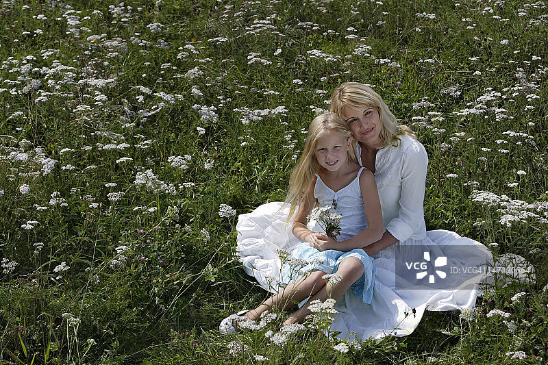 母亲和女儿坐在鲜花草地上图片素材