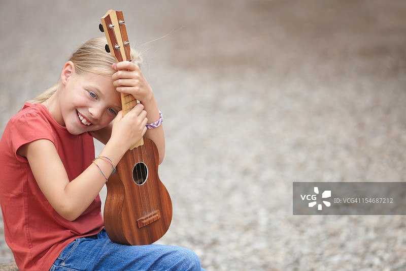 年轻的金发女孩摆着她的四弦琴，微笑着图片素材