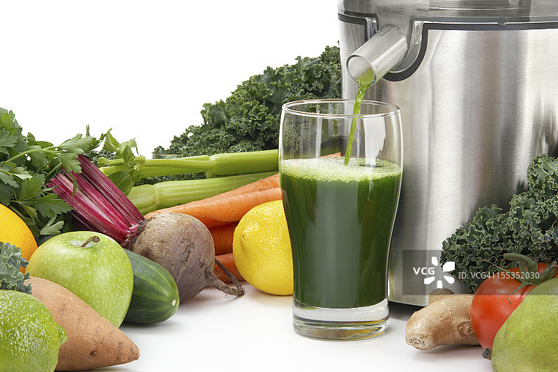 榨汁机将果汁倒入被蔬菜包围的玻璃杯中图片素材