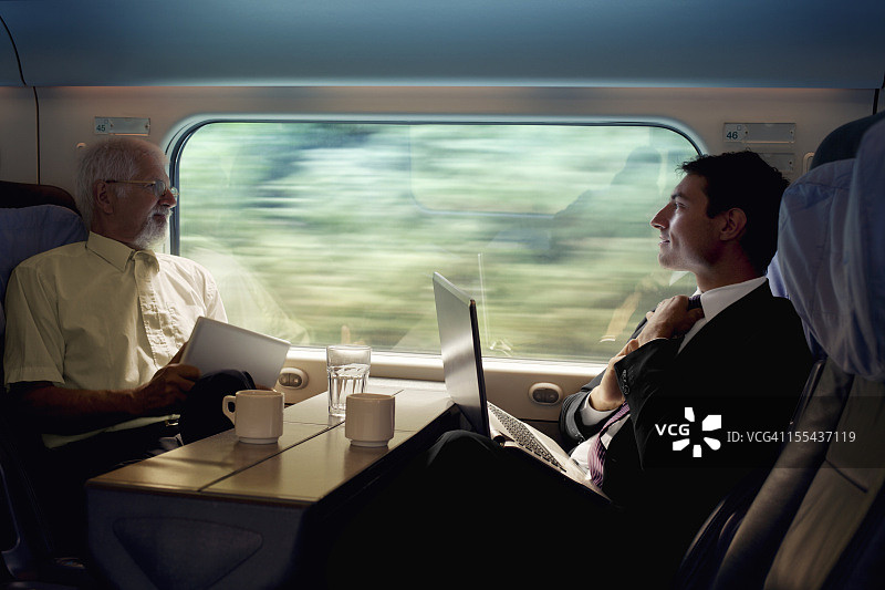 两个商人坐在火车靠窗的位置上工作图片素材
