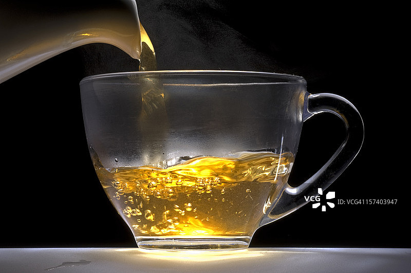 茶水从白色瓷壶倒入玻璃杯中。图片素材