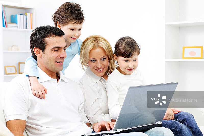 快乐的四口之家，坐着笔记本电脑。图片素材