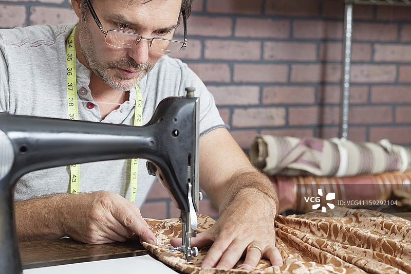 成熟的男裁缝在缝纫机上缝制布料图片素材
