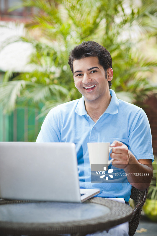 一个拿着一杯咖啡在笔记本电脑上工作的男人图片素材
