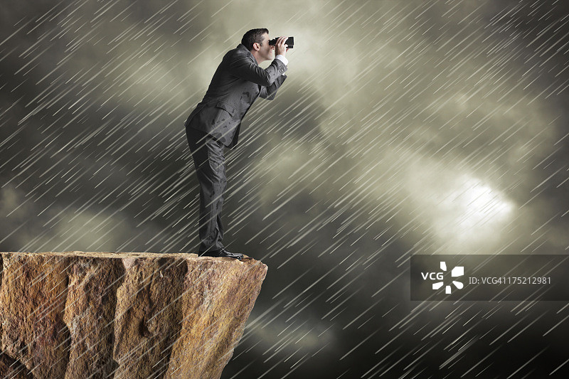 一名商人站在悬崖上，用双筒望远镜看雨图片素材