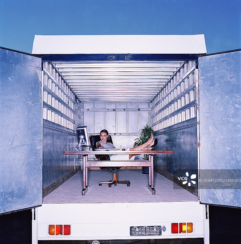 脚踏在卡车后面办公桌上的女商人图片素材