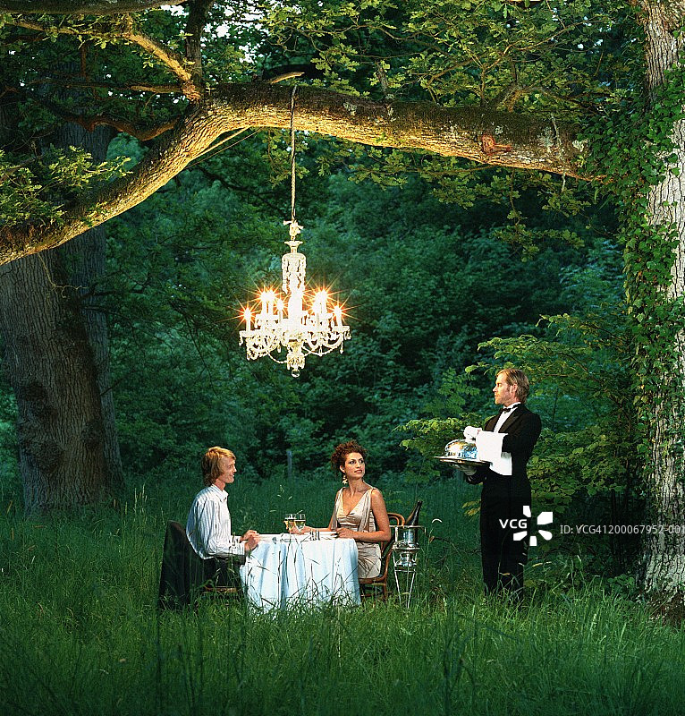 在森林里的餐桌上服侍年轻夫妇的管家图片素材