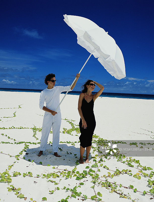 一个年轻人在沙滩上为一个女人撑阳伞图片素材