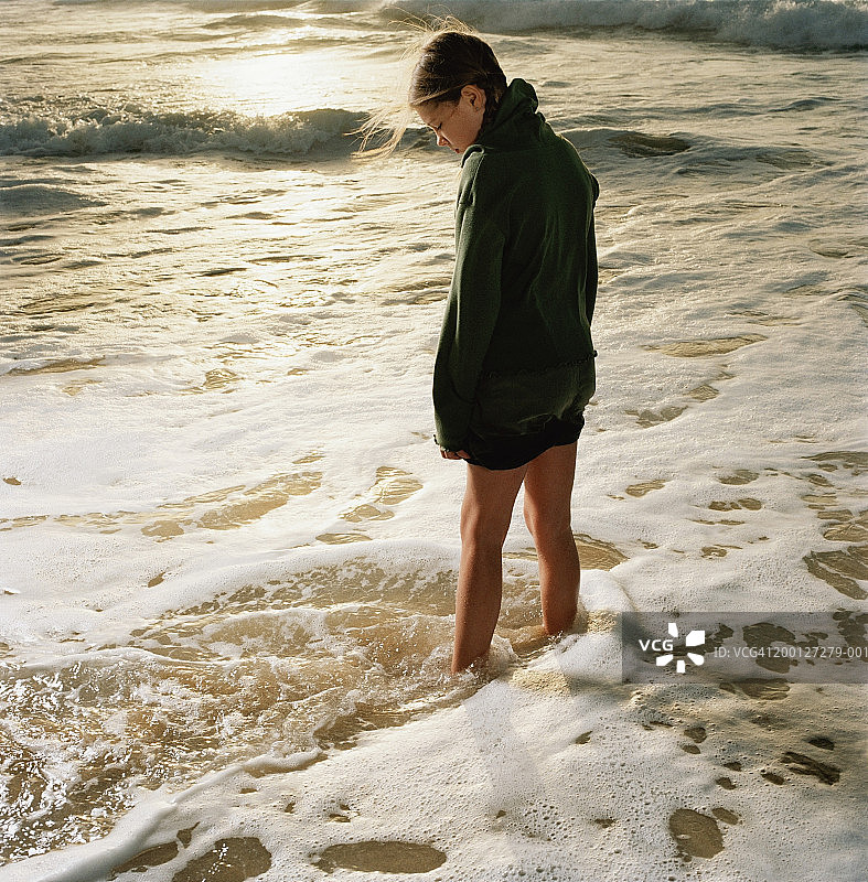 女孩(6-8)站在海滩上，海浪冲刷着脚图片素材