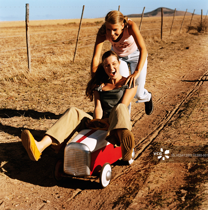 两个女人在玩卡丁车，一个推着另一个在土路上走图片素材