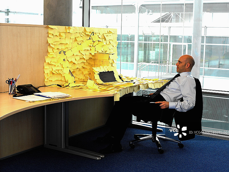 一名男子坐在堆满黄色便笺的办公桌前图片素材