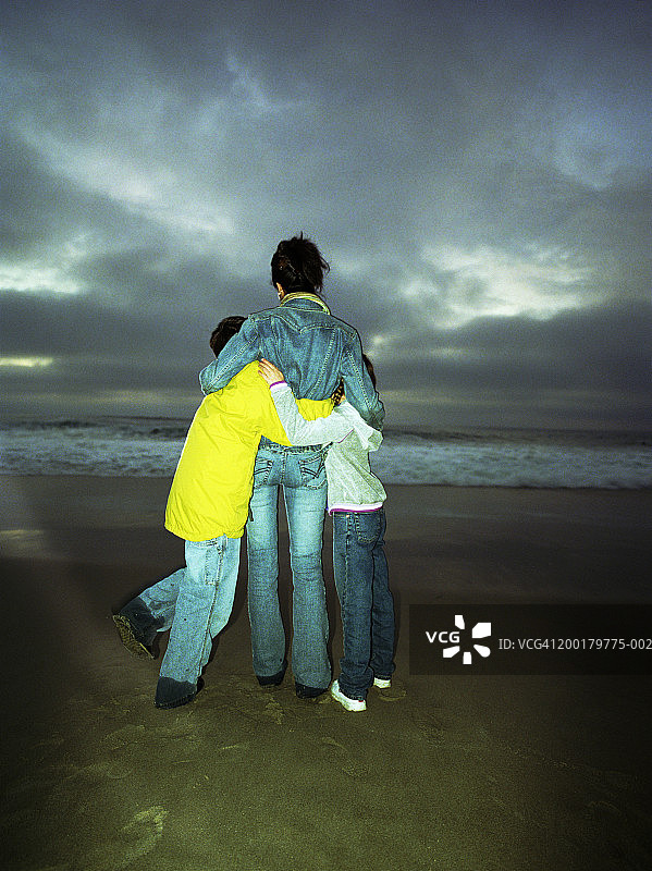 母亲拥抱孩子(6-12)在海滩，后视图图片素材