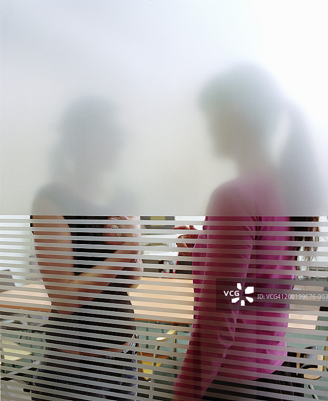两个女商人站在会议室里，透过玻璃观看图片素材